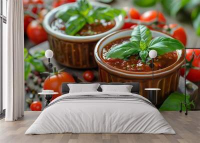 Two small bowls of tomato sauce with basil on top of them and tomatoes around them on a wooden Wall mural