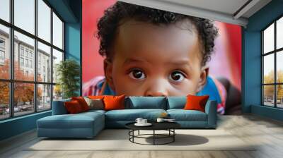 A young boy with curly hair looks intensely at the camera while sitting on a playground slide. Wall mural