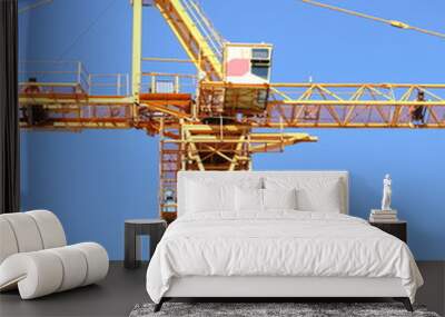 The cabin of a yellow tower crane is high in the blue sky Wall mural