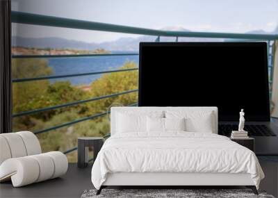 Laptop with blank screen on the balcony overlooking the sea and mountains. summer vacation. work place. Wall mural