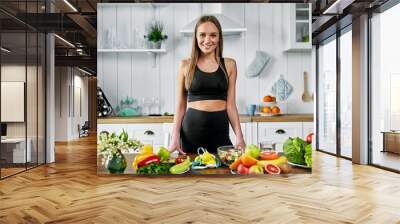 A sporty girl stands in the kitchen near a table with fruits and other useful foods. Healthy eating concept Wall mural