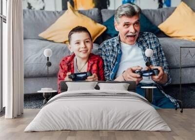 Active inspired man and his grandson enjoying new video game.. Sit on floor in living room. Wall mural