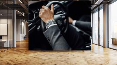 Close up top view of  man's watch in black suit keeping hand on the steering wheel while driving a luxury car. Wall mural