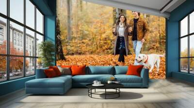 Family and hot autumn drink, couple in love holding cups of tea or coffee and holding hands, walking with dog. Wall mural