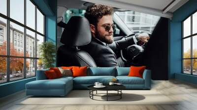 Portrait of handsome young businessman in full suit in sunglasses driving a new car. View from behind. Wall mural