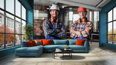 Two young builders in working uniform and helmets crossed arms. Wall mural