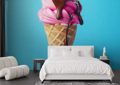 Pink ice cream cone topped with chocolate drizzle and colorful sprinkles on a blue background Wall mural