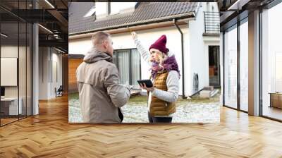 Portrait of two people dark-hared man back and blonde hair woman in hat with calculator holding pencil in air near house Wall mural