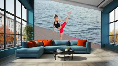 Beautiful young slim girl doing yoga or gymnastic exercise by the lake. Healthy lifestyle. children's sports concept. Wall mural