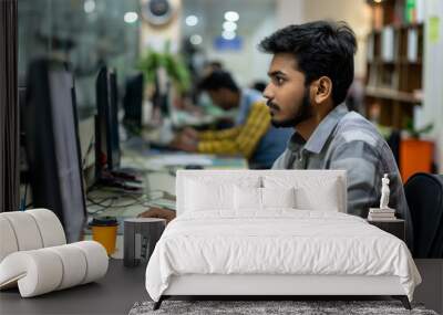 Indian employee focuses on his computer in a busy office setting, showcasing a modern workplace in India Wall mural