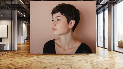 Profile view of a young woman showcasing her stylish pixie cut against a soft pink background Wall mural