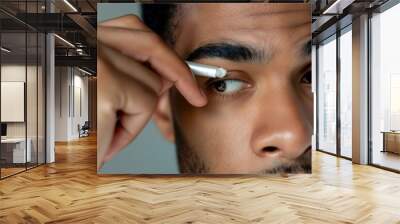 Young adult man applying under-eye cream for skincare routine and facial treatment to prevent dark circles and signs of aging Wall mural