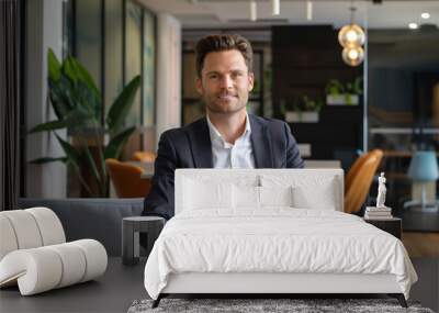 Young businessman is sitting on a sofa in a modern office, looking relaxed and confident Wall mural