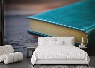 A closed book with a teal cover on a wooden surface Wall mural