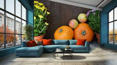 Two apples and two orange pumpkins on background of old brown wooden board with yellow and purple chrysanthemums flowers. Autumn harvest, Thanksgiving Day or Halloween concept. Wall mural