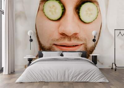 Relaxed bearded young man in a towel on his head being in spa salon with moisturizer cucumber and mask on the face Wall mural