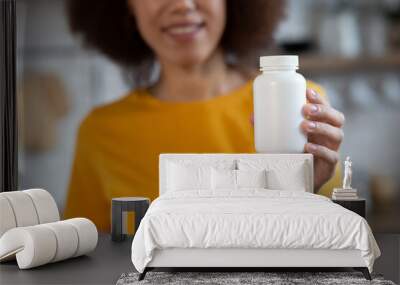 Happy young smiling African American woman holding bottle of dietary supplements or vitamins in hands, close up. selective focus. Healthy lifestyle concept Wall mural