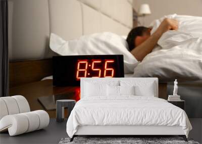 Alarm clock on bedside table with red numbers, kitchen knife, sleeping man in bed in room. Concept chef sleeping after hard day at restaurant, sleep disturbance, oversleep work, night shift Wall mural