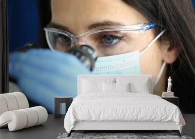 Portrait of woman in mask and glasses looks through microscope. Research and testing of new approaches in medicine concept Wall mural