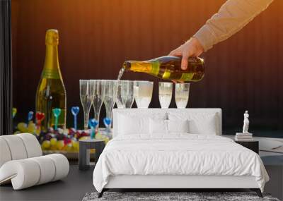 A man is pouring champagne to the glasses. Party table with fruit plate on. Wall mural