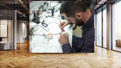 A young man at a desk in the workshop of a dental technician in the laboratory makes parts for dentistry Wall mural