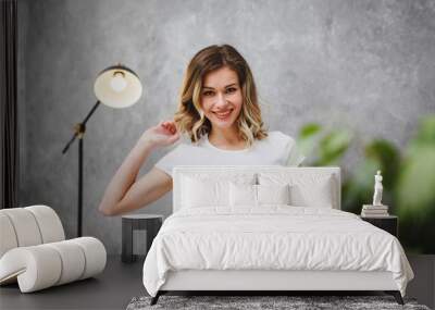 Portrait of a young beautiful woman on a gray background. A cute girl in a white T-shirt looks at the camera and smiles, close-up. Wall mural