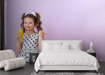 A little girl holds an orange juice and points to an advertisement on an isolated pink background. Copy space. Wall mural