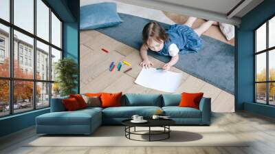 A two-year-old girl lies on the floor and draws with pencils. Living room with modern interior. View from above. Kids creative activity. Wall mural