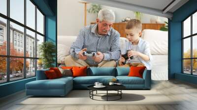 Happy family. Old senior man grandfather boy grandson playing video game with joysticks at home. Smiling grandparent and child using gamepads for video game. Older generation modern tech usage Wall mural