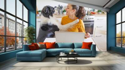 Mobile Office at home. Young woman with pet dog sitting in kitchen at home working using on laptop computer pc. Lifestyle girl studying indoors. Freelance business quarantine concept. Wall mural