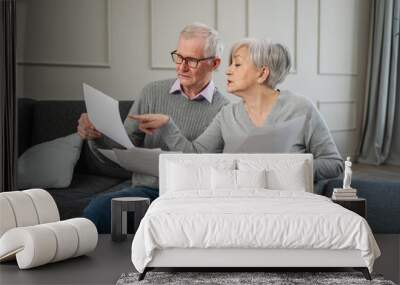 Sad tired disappointed middle aged senior couple sit with paper document. Unhappy older mature man woman reading paper bill managing bank finances calculating taxes planning loan debt pension payment Wall mural