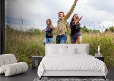 Summer holidays vacation happy people concept. Group of three friends boy and two girls running and having fun together outdoors. Picnic with friends on road trip in nature. Wall mural