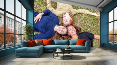 Summer holidays vacation happy people concept. Top view group of three friends lying on grass in circle smiling and having fun together outdoors. Picnic with friends on road trip in nature. Wall mural