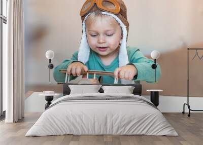 A handsome little boy of 2 years old in a pilot's hat is playing with a wooden airplane and a logistics constructor. Children's wooden toys for child development. Wall mural