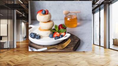 Cottage cheese pancakes, Russian cheesecakes with fresh blueberries, strawberries, honey and mint leaves on a stylish wooden board on a gray concrete table.  Healthy and delicious breakfast. Wall mural