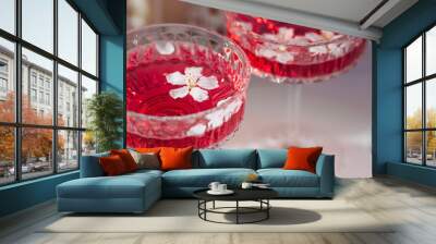 Two fashionable glasses for dessert and champagne with a pink drink and cherry blossoms inside on a light background with hard shadows and highlights. The concept of a party and a holiday. Wall mural