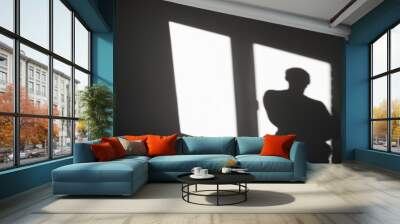 Silhouette of a man on reflected light from a window on a gray wall. Abstract background with shadow of a man. Wall mural