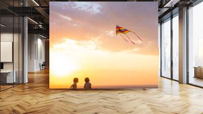 two happy little kids boys having fun with kite in nature at sunset Wall mural