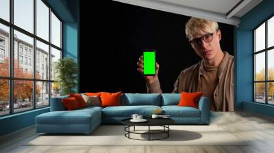 guy 25 years old holds in his hand a smartphone mockup with a chroma key screen on a black background Wall mural