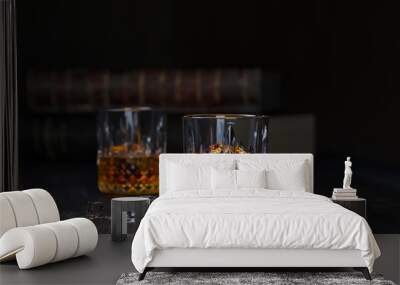 whiskey two glasses with ice, stand on a dark old wooden table with old books on a black background Wall mural