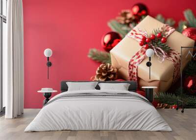 Christmas gift is surrounded by red christmas ornaments and pine branches on red background Wall mural