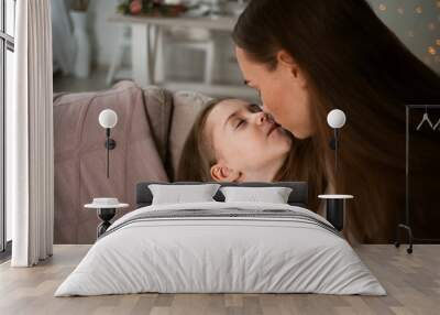 portrait of a mother kissing her little daughter on the sofa in the room Wall mural