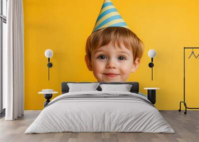 A cheerful young boy wearing a striped blue party hat smiles brightly against a vibrant yellow background Wall mural