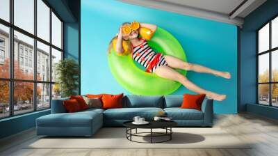 A cute little girl is smiling and holding orange slices in front of her eyes. Isolated blue background. Summer vacation concept Wall mural