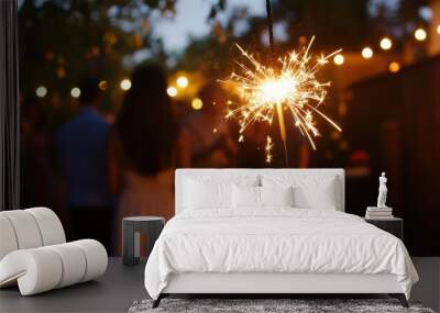 A person holds a sparkler while friends celebrate at an outdoor gathering during twilight in a festive atmosphere Wall mural