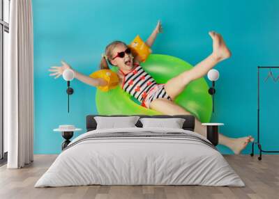 Happy little child girl in a swimwear suit lying on a bright inflatable circle. Blue background. Top view. Summer and vacation concept Wall mural