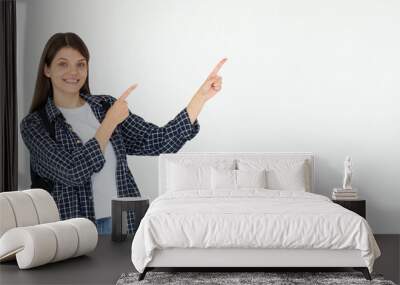 Hey look. Smiling pretty female model pointing fingers right at empty space and inviting to check it out, showing advertisement on white background. Wall mural