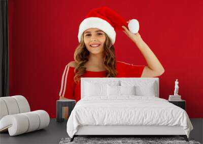 Merry fun young woman wear red dress posing look camera hold in hand show Santa hat pompon isolated on red background. Happy New Year 2025 celebration holiday concept Wall mural