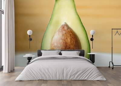 Half a fresh green avocado stands isolated in the middle on a plate on a wooden background. Close-up. Wall mural