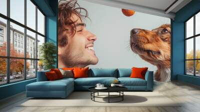 A person with a joyful expression, playing with a pet dog and throwing a ball with laughter and happiness against a white backdrop. Wall mural